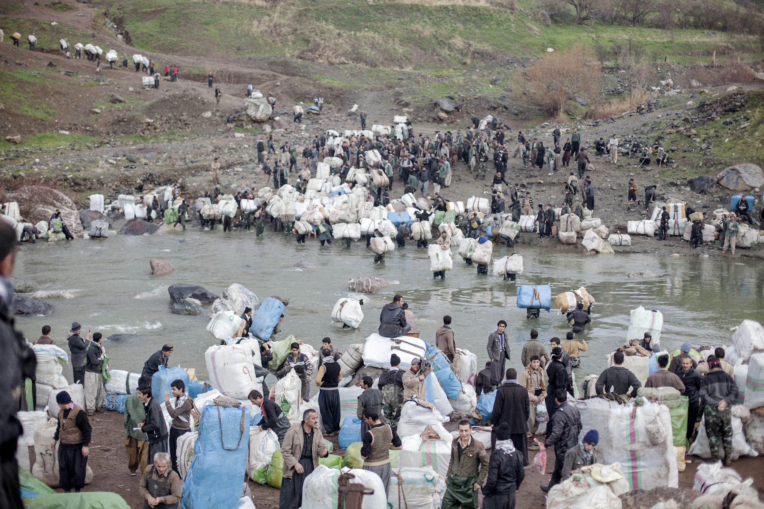 Pašeráci přechází přes řeku Šabaddin, která tvoří hranici mezi Irákem a Íránem. Íránští vojáci pašeráky sledují zpovzdálí poté, co dostali bakšiš, aby nedělali potíže. Šabaddin, irácký Kurdistán, íránsko-irácká hranice, prosinec 2014.