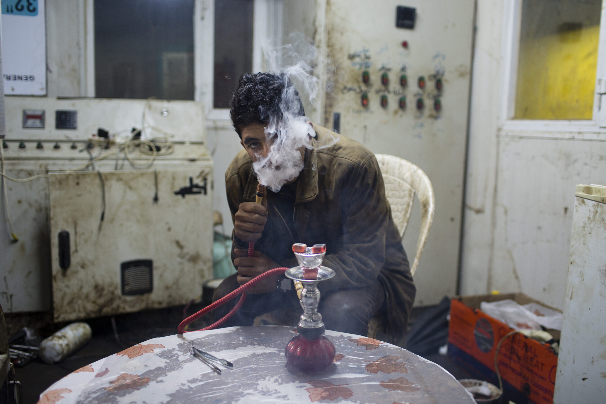 Vysídlený jezíd ze Sindžáru, kouří tabák s vonnou příměsí z malé vodní dýmky v provizorní boudě. Tandžero, Džamal, Irák, únor 2015.