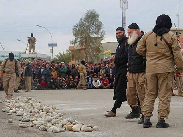 Bojovníci IS si připravují kameny na kamenování dvacetileté ženy, kterou skupinově znásilnili a následně obvinili z cizoložství.
